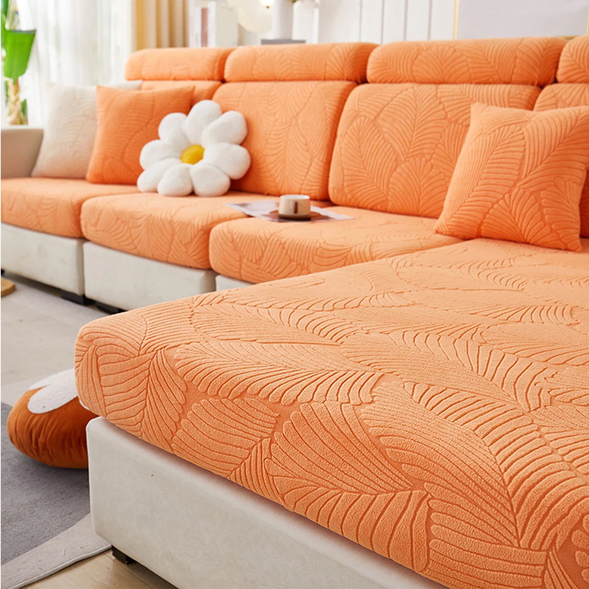 An orange leaf jacquard stretch sofa cover with anti-slip backing displayed on a modern sofa.