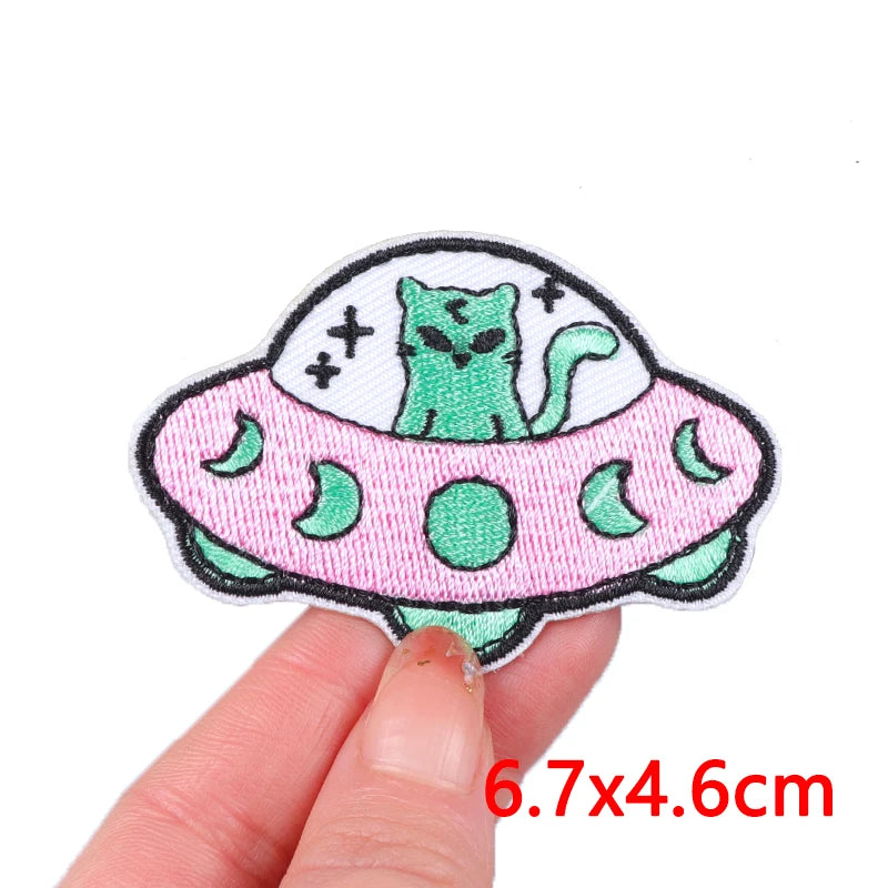 An embroidered patch featuring a green cartoon cat inside a pink, ring-shaped design.