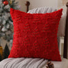 A red textured corduroy throw pillow with embroidered Christmas tree designs resting on a gray knitted blanket.