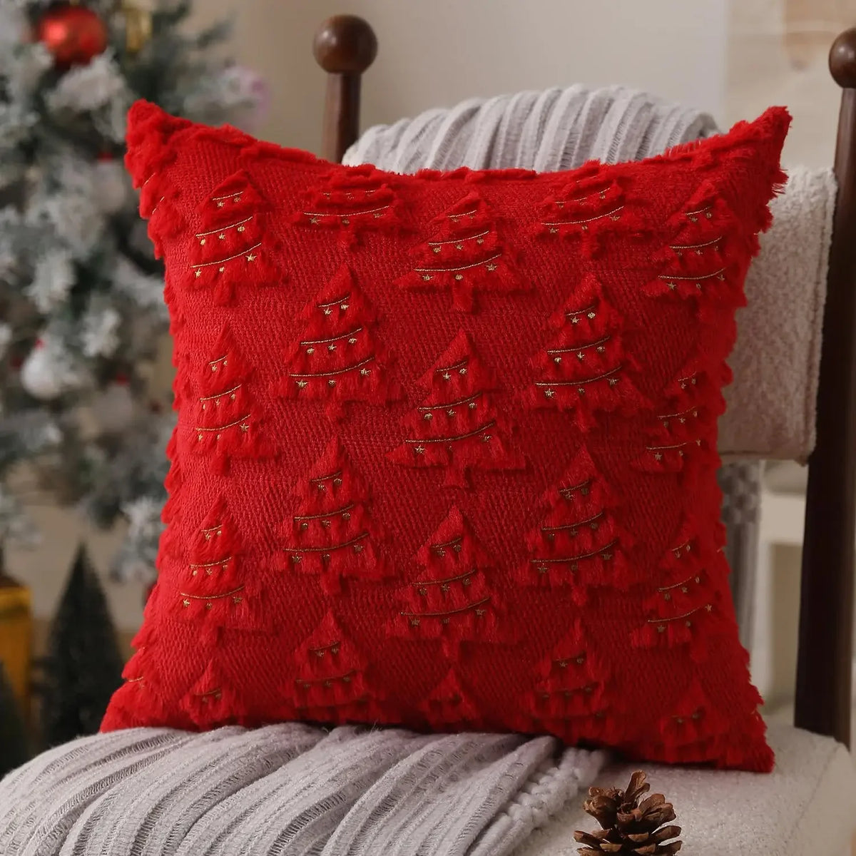A red textured corduroy throw pillow with embroidered Christmas tree designs resting on a gray knitted blanket.