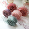 A collection of pink, mauve, and mint green silky organza ribbon rolls for gift wrapping and crafts.