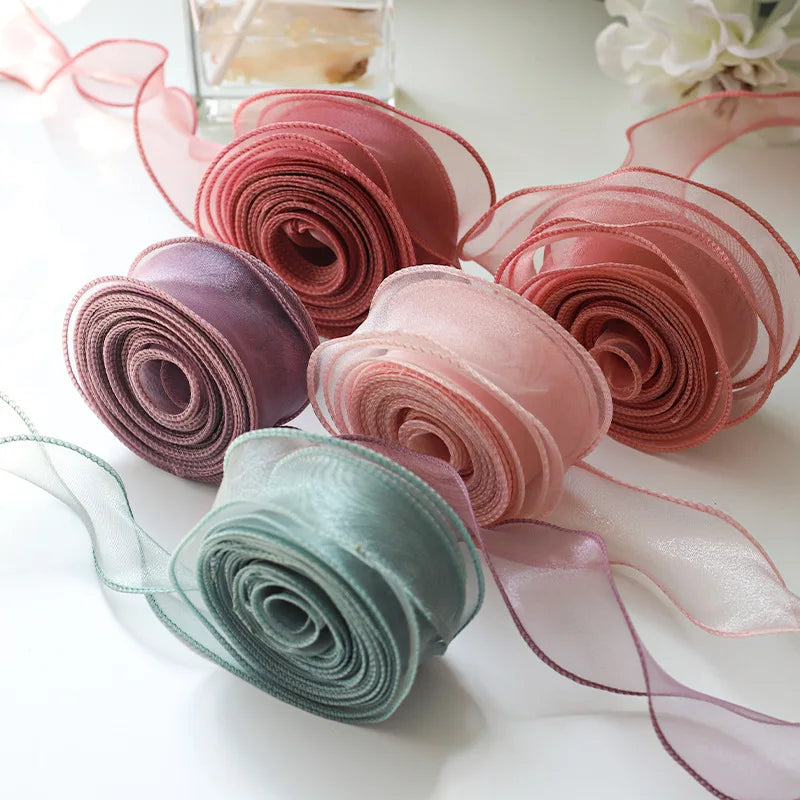 A collection of pink, mauve, and mint green silky organza ribbon rolls for gift wrapping and crafts.