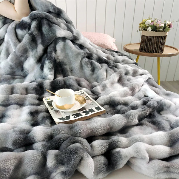 A plush rabbit fur throw blanket in shades of gray and white draped over a surface with a cup and saucer.