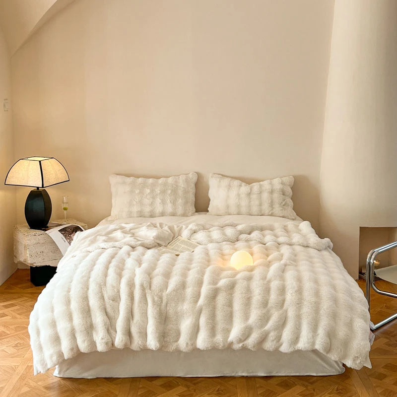 A fluffy cream faux fur throw blanket is displayed on a bed with soft lighting.