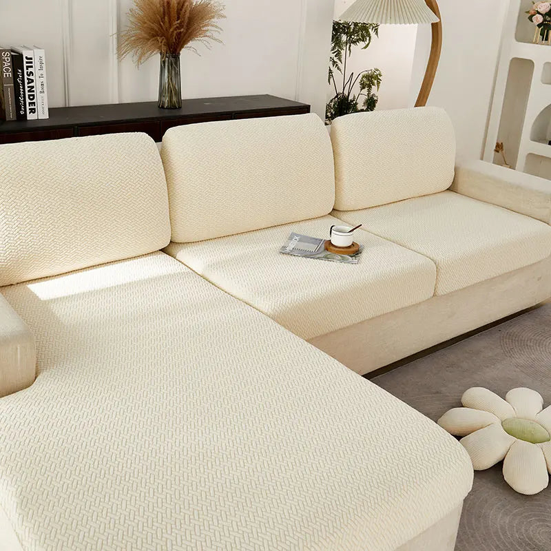 A light cream jacquard knit sofa cushion cover on a beige sofa with a dark wood table and greenery.