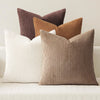 A set of four textured throw pillows in shades of brown, beige, and cream arranged on a light surface.