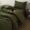 A close-up of a dark olive green duvet cover set with matching pillows and a folded throw on a bed.