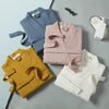 A collection of three knitted cotton terry robes in light blue, pink, and white laid out on a gray surface.