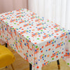 A white disposable plastic tablecloth with a colorful birthday pattern is spread on a table.