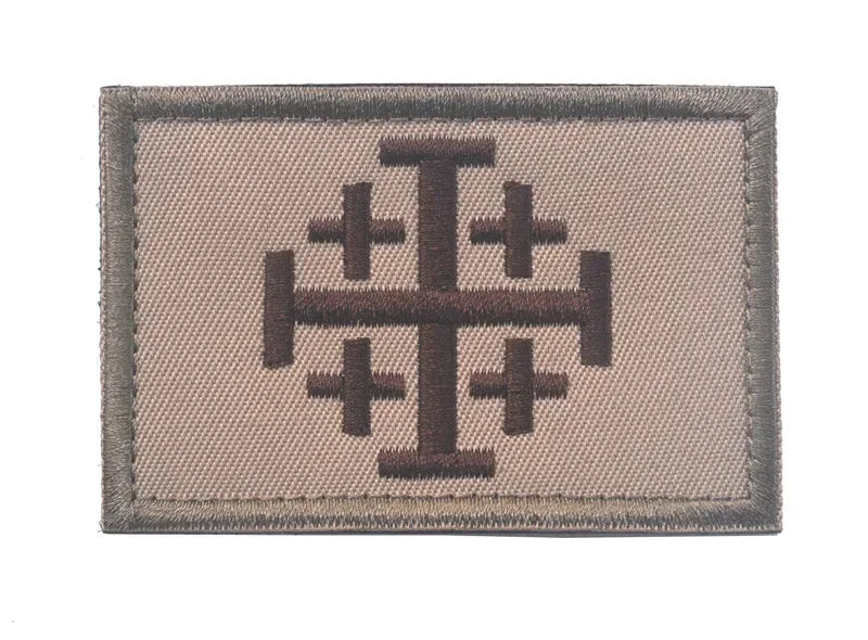 A rectangular embroidered patch featuring a dark brown cross design on a light beige fabric background.