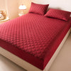 A red quilted mattress protector is shown on a bed, featuring a diamond pattern.