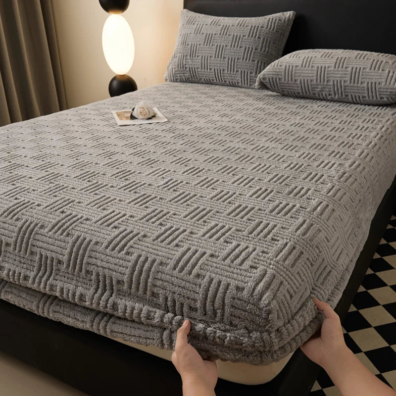 A gray plush jacquard mattress cover is shown on a bed, with pillows and a bedside lamp visible.