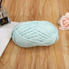A ball of light mint green flat thread yarn is displayed on a wooden surface next to a small glass container.