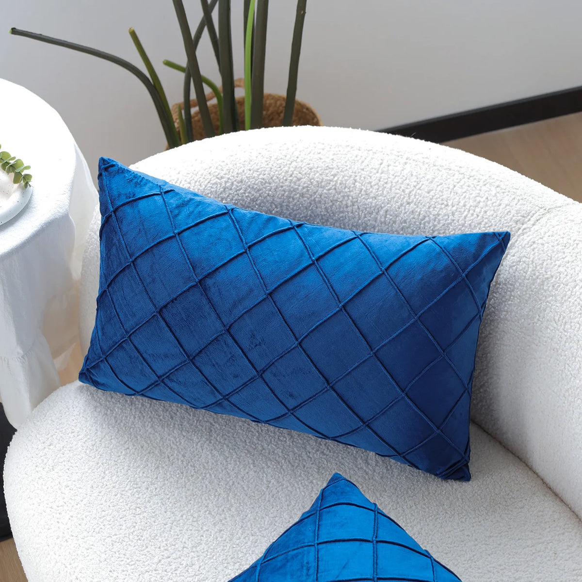 A deep blue quilted velvet decorative pillow on a white sofa with a matching pillow nearby.
