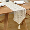 A cream colored vintage crochet lace table runner with fringe placed on a wooden table.