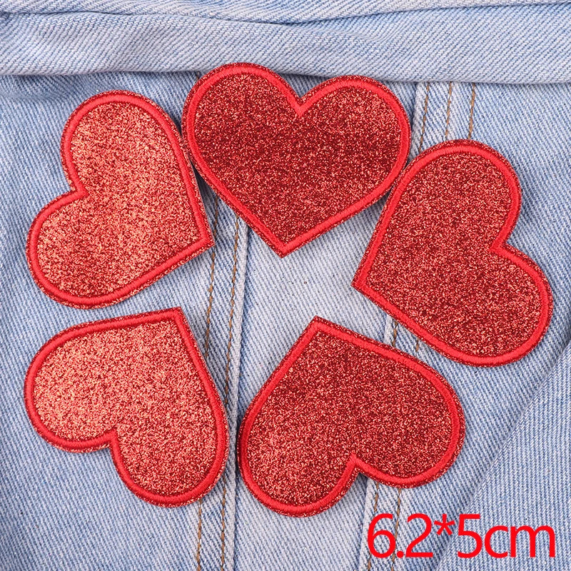 Five red glitter heart patches sewn onto a denim fabric.