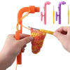 A hand is using an orange crochet tool to manipulate a yarn, with various pink and yellow tools displayed nearby.