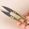 A pair of silver-toned U-shape sewing scissors with dark blades are held in a hand.