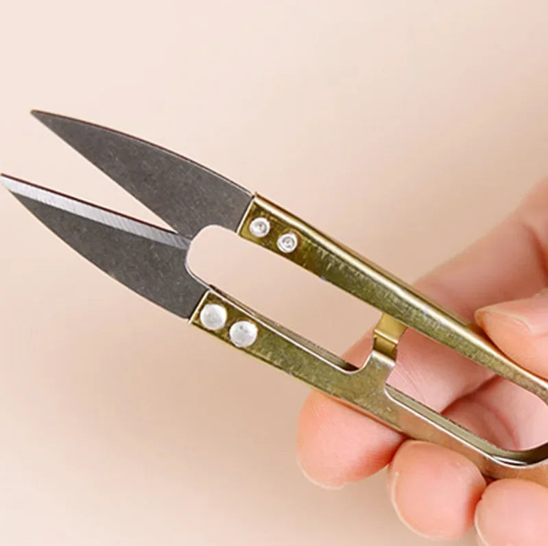 A pair of silver-toned U-shape sewing scissors with dark blades are held in a hand.