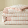 A stack of pink and white striped luxury jacquard summer quilts folded neatly.
