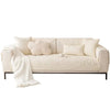 A cream colored sofa cover with textured pillows and a white throw blanket on a light wood frame.