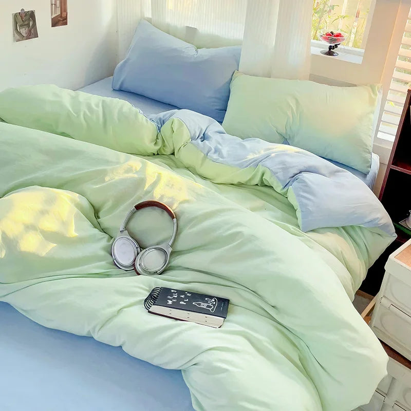 A light green cotton bed linen set with blue accents is spread on a bed, illuminated by natural light.