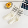 A pair of white and gray striped crew socks lying next to a golden donut on a white desk.