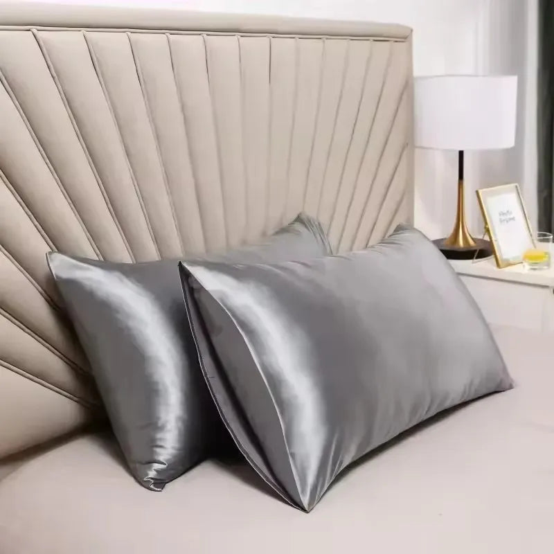 A close-up of a silver satin pillowcase with a quilted headboard and a white lamp on a bedside table.