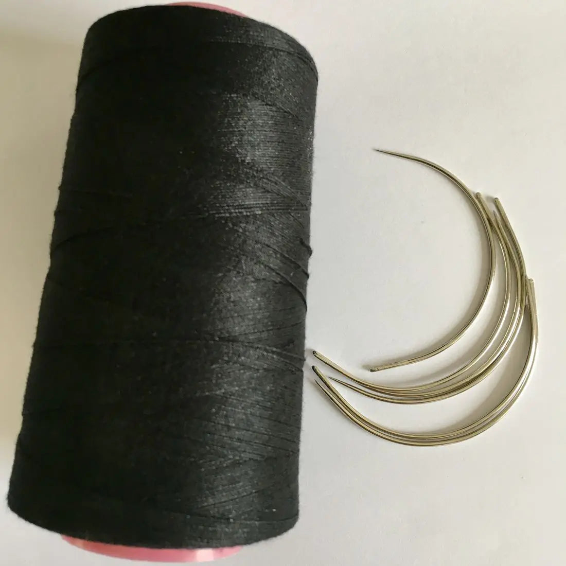 A roll of black cotton hair weave thread with several loose strands unwound beside it.