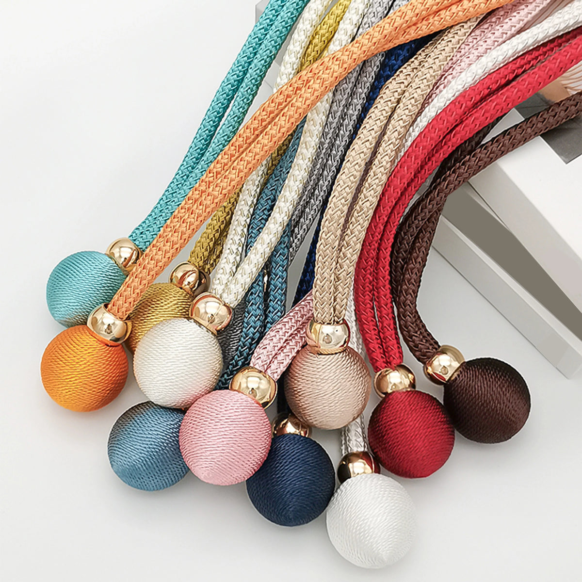 A collection of colorful, textured cord tiebacks in various shades of orange, green, brown, and gray.