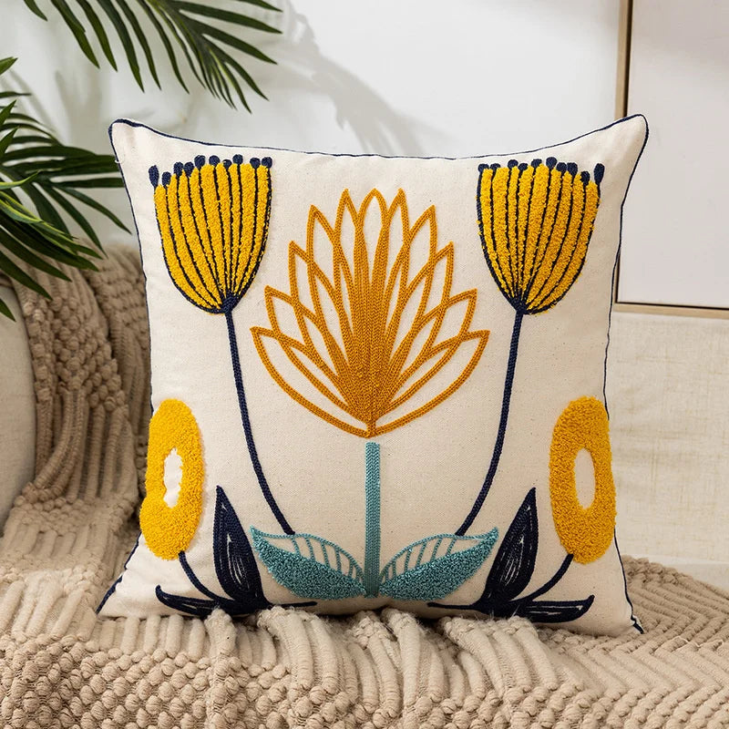 A cream-colored throw pillow cover embroidered with yellow and orange floral designs on a neutral beige knitted surface.