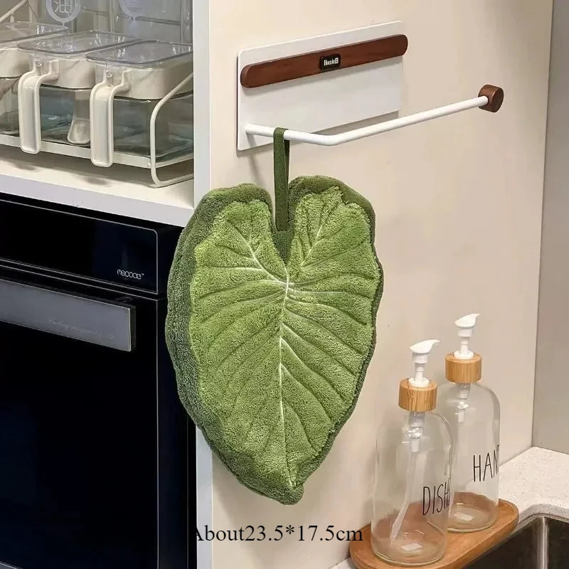 A green embroidered leaf hand towel hanging on a wall next to a black appliance.