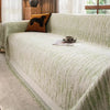 A light green textured sofa cover blanket draped over a sofa with an orange throw pillow.