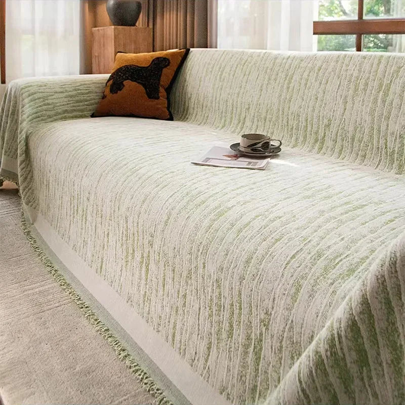 A light green textured sofa cover blanket draped over a sofa with an orange throw pillow.