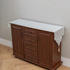 A wooden cabinet with a white embroidered lace table runner on top, used for dining or furniture accents.