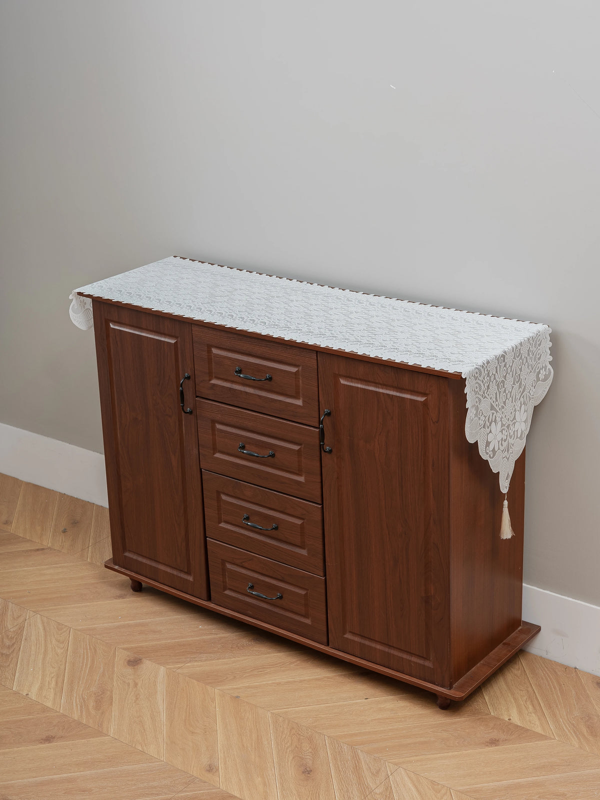 A wooden cabinet with a white embroidered lace table runner on top, used for dining or furniture accents.