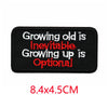 Black iron-on embroidered letter patch with red text that reads Growing old is inevitable growing up is optional