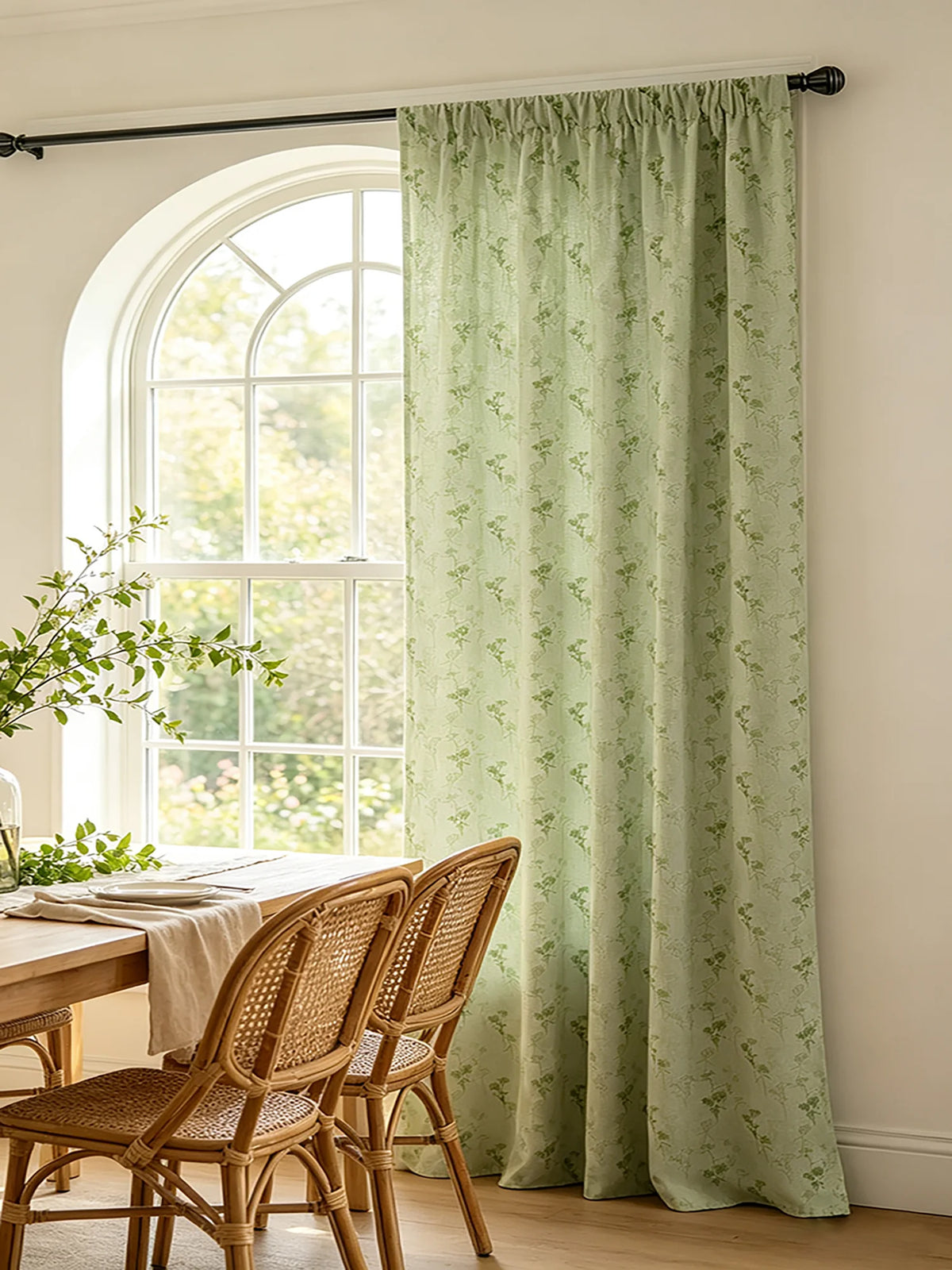 Sage green floral print curtains hanging in a window with wooden furniture and greenery visible.