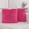 Two bright pink faux fur throw pillows resting on a white sofa.