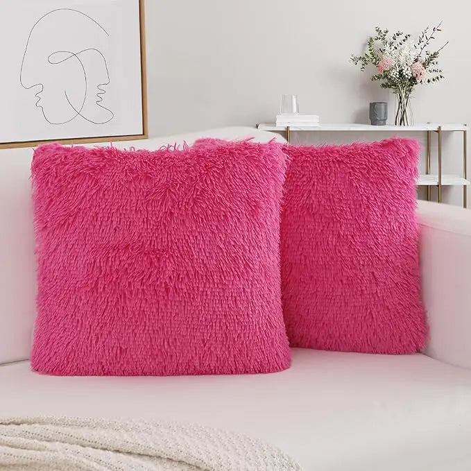 Two bright pink faux fur throw pillows resting on a white sofa.