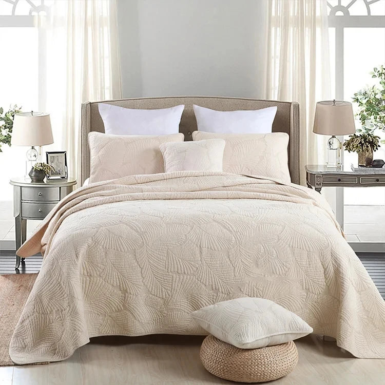 A beige embroidered cotton quilted pillow cover set displayed on a bed with white linens and light curtains.
