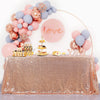 A pink and blue balloon decoration setup with a 'love' sign and a gold tiered cake on a sequin table cover.