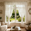 A pair of sheer white curtains with ruffled lace trim hang over a window in a bright room.