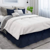 A queen bed dressed with a navy blue skirt and white bedding featuring patterned pillows.