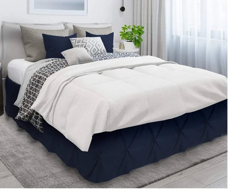 A queen bed dressed with a navy blue skirt and white bedding featuring patterned pillows.
