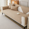 A beige quilted anti-slip sofa cover with plush texture on a white sofa in a bright room.