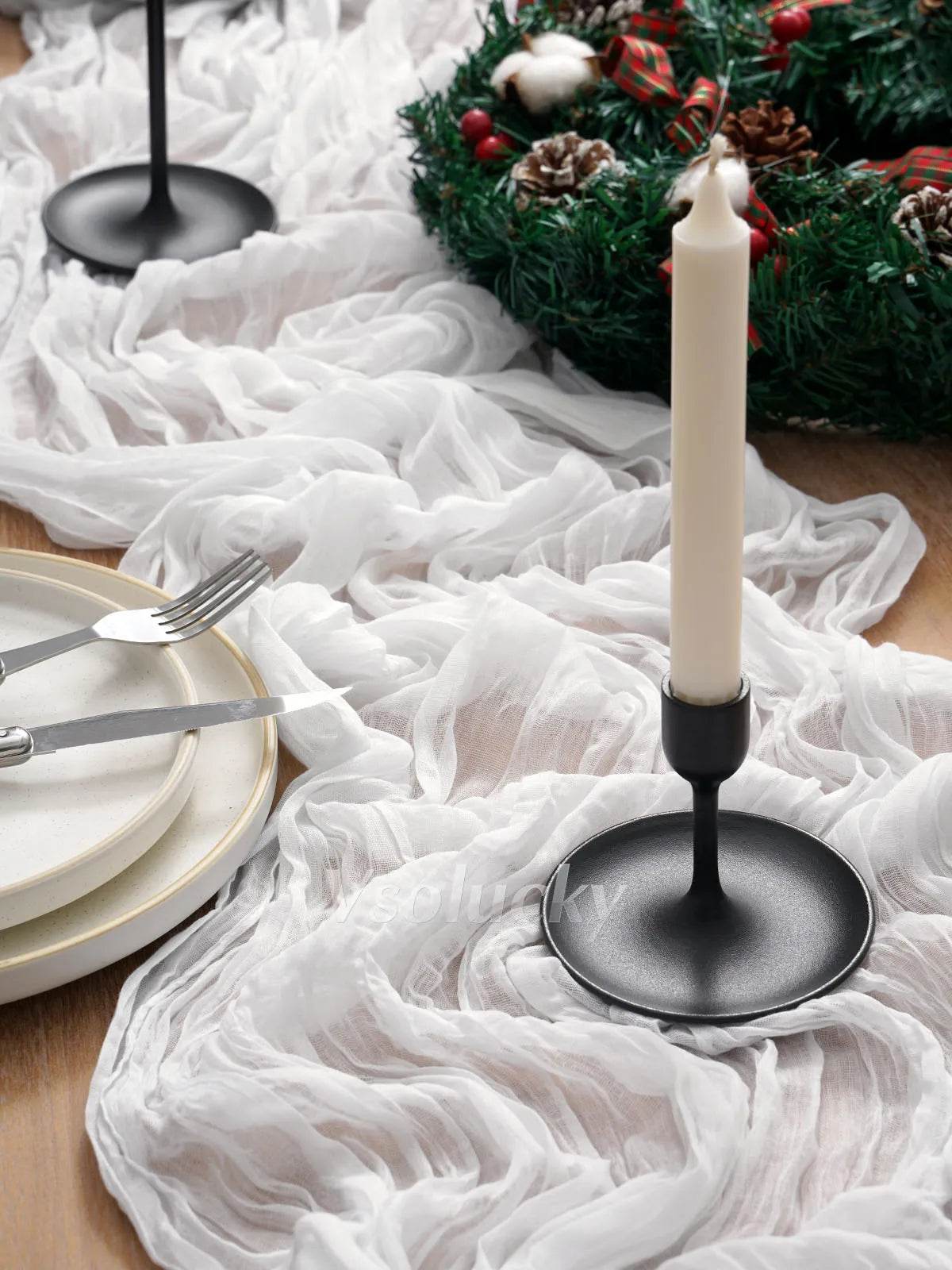 A white crinkle cheesecloth table runner is displayed on a wooden surface with silverware and a tall white candle.