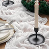 A white crinkled cheesecloth table runner is displayed on a wooden surface with silverware and a tall white candle.