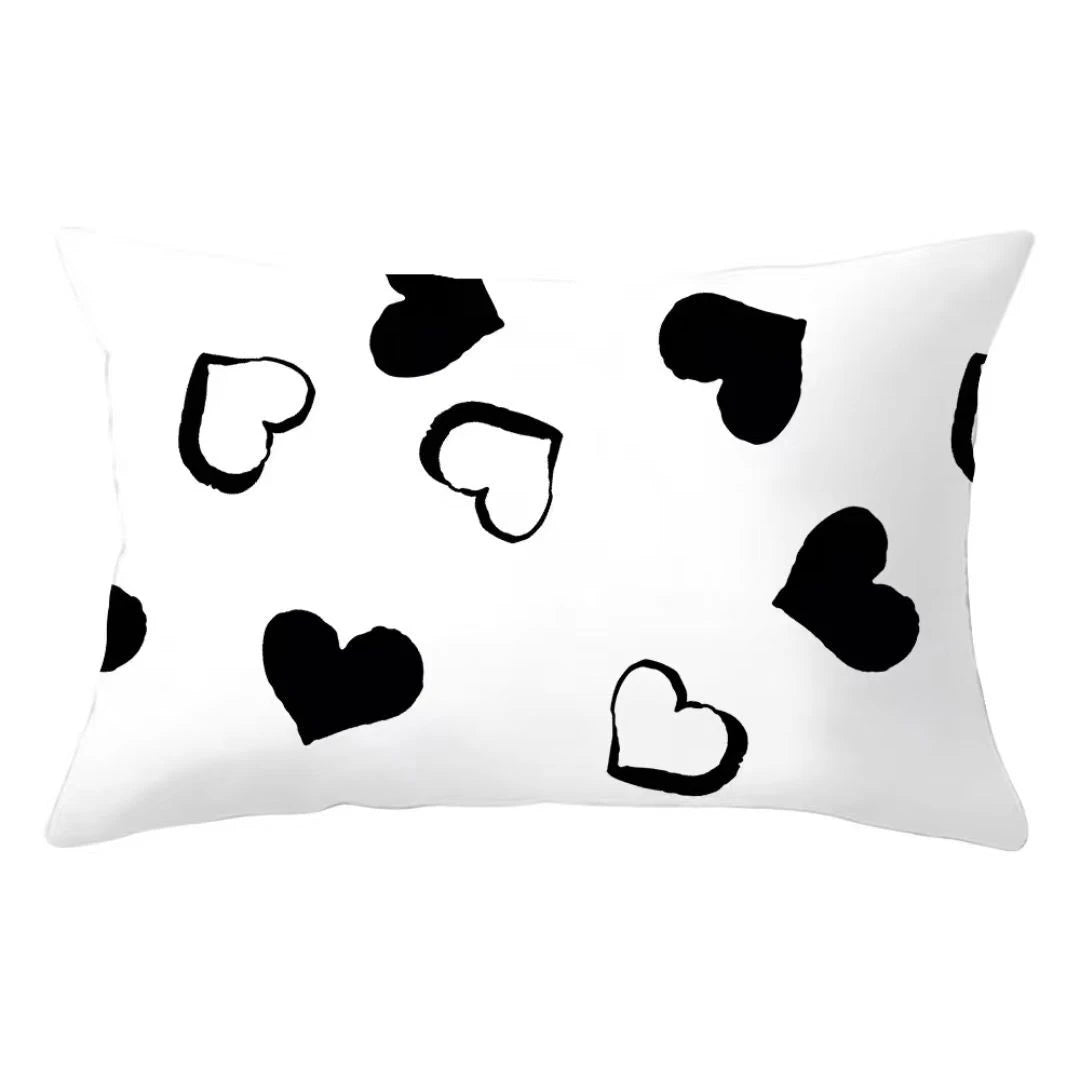 A white decorative pillow cover featuring a pattern of black heart shapes.