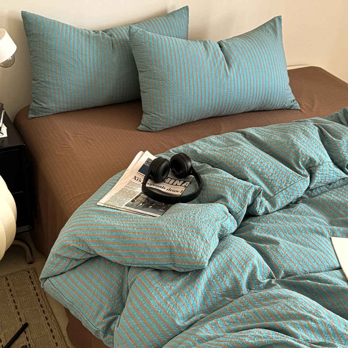 A striped teal duvet cover set is displayed on a bed with brown bedding and a dark nightstand.